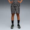 Sur fond gris, un modèle pose en short à motifs, haut assorti, chaussettes noires et chaussures de foot.