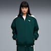 Ein Model posiert vor grauem Hintergrund und trägt eine grün-weiße Puma-Jacke.