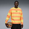 A model poses against grey holding a basketball, wearing a striped orange and yellow jumper.