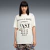 Een model staat tegen een grijze achtergrond, gekleed in een T-shirt met slogan en een short met print.