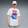 Een model staat tegen een grijze achtergrond met een pet en een wit T-shirt met autoafbeeldingen.