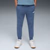 Een model staat op een grijze achtergrond, gekleed in een blauwe joggingbroek en witte sportschoenen.