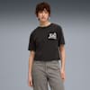 Vor grauem Hintergrund trägt ein Model ein dunkles T-Shirt mit Grafik und graue Jeans.