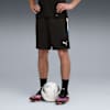 Ein Model steht mit einem Fußball, trägt schwarze Shorts, Socken und bunte Fußballschuhe.