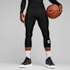 Een model houdt een basketbal vast tegen een grijze achtergrond, gekleed in zwarte sportkleding en sneakers.