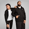 Zwei Models posieren vor grauem Hintergrund, tragen schwarze Trainingsanzüge und weiße T-Shirts.