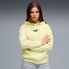 Na szarym tle modelka ze skrzyżowanymi ramionami w jasnożółtej bluzie z kapturem z logo Puma.