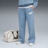 Sur fond gris, un modèle pose avec un pantalon bleu, des baskets et un sac.