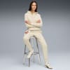 On grey, a model sits with arms crossed, wearing a cream hoodie and jogging bottoms.