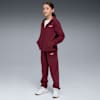 Een model met een grijze achtergrond draagt een bordeauxrood trainingspak en witte sneakers.