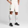 Een model poseert tegen grijs in witte shorts, sokken met groen-rode details en zwarte schoenen.