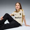 Un modello è seduto su uno sfondo grigio, indossa una maglietta color crema e oro e jeans scuri.
