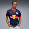 Een model poseert tegen een grijze achtergrond, gekleed in een blauw Red Bull Salzburg T-shirt.