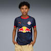 Ein Kind posiert vor grauem Hintergrund in einem marineblauen Fussballtrikot mit roten Details.