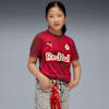 Vor grauem Hintergrund posiert ein Model in rotem Red Bull T-Shirt und grauen Shorts.