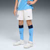 Su uno sfondo grigio, un modello indossa un kit da calcio con calzini azzurri e scarpe bianche.