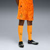 Op grijs draagt een model oranje AC Milan-tenue met sokken en zwarte voetbalschoenen.