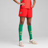 Vor grauem Hintergrund posiert ein Model in roter Hose, grünen Socken und Fußballschuhen.
