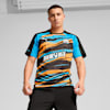 Ein Model steht vor grauem Hintergrund und trägt ein gemustertes Olympique de Marseille T-Shirt.