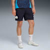 Tegen een grijze achtergrond draagt een model een marineblauwe short, sokken en sportschoenen.
