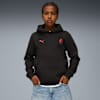 Against grey, a model poses wearing a black hoodie, with red logos and blue jeans.