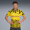 Un modèle pose sur fond gris avec un maillot de foot jaune et noir du Borussia Dortmund.