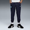 Een model staat tegen een grijze achtergrond, gekleed in een joggingbroek en zwart-witte sneakers.