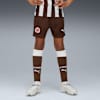 Op grijs draagt een model een St. Pauli-tenue: bruine shorts, sokken en witte hardloopschoenen.