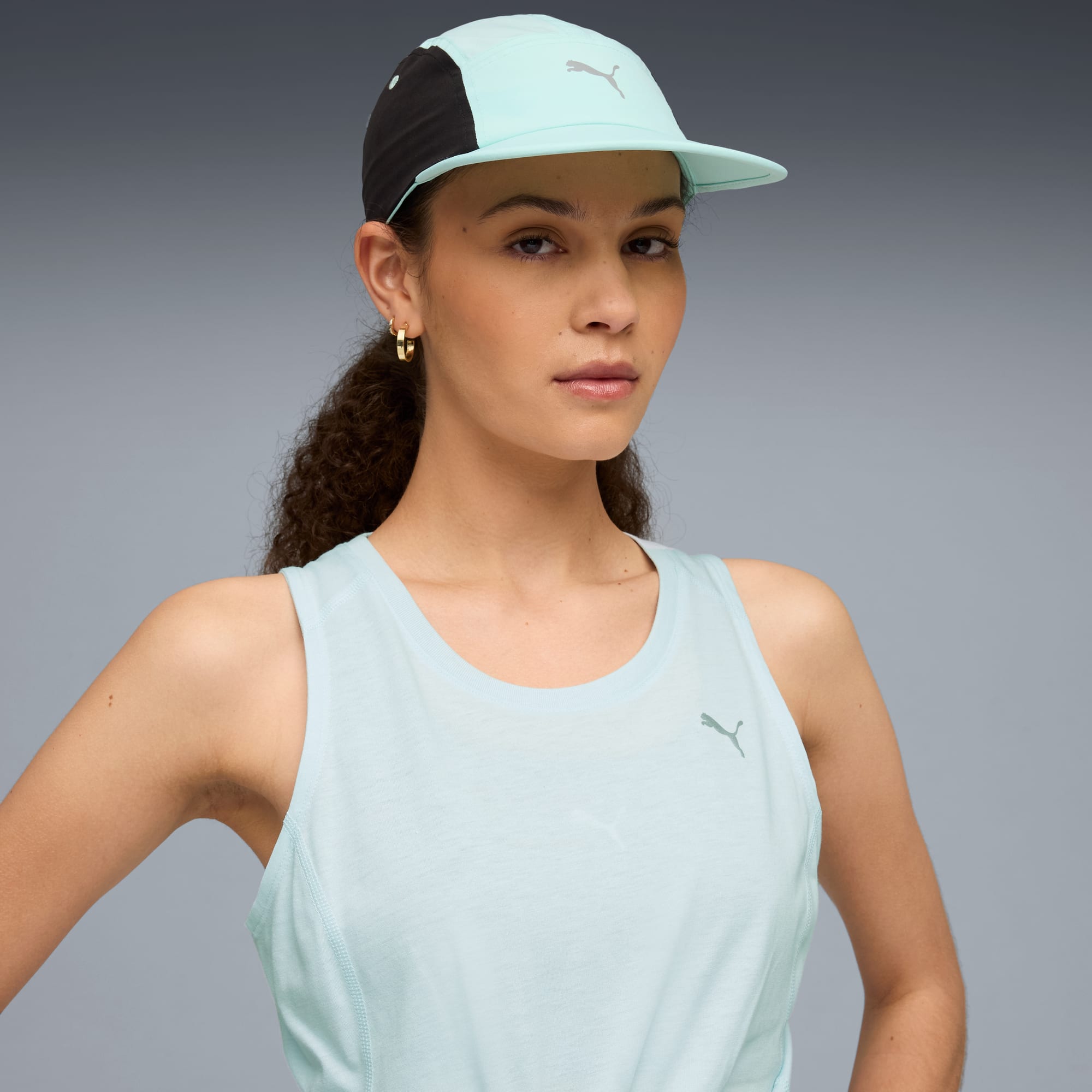 Su sfondo grigio, una modella guarda la fotocamera indossando top e cappellino azzurri.
