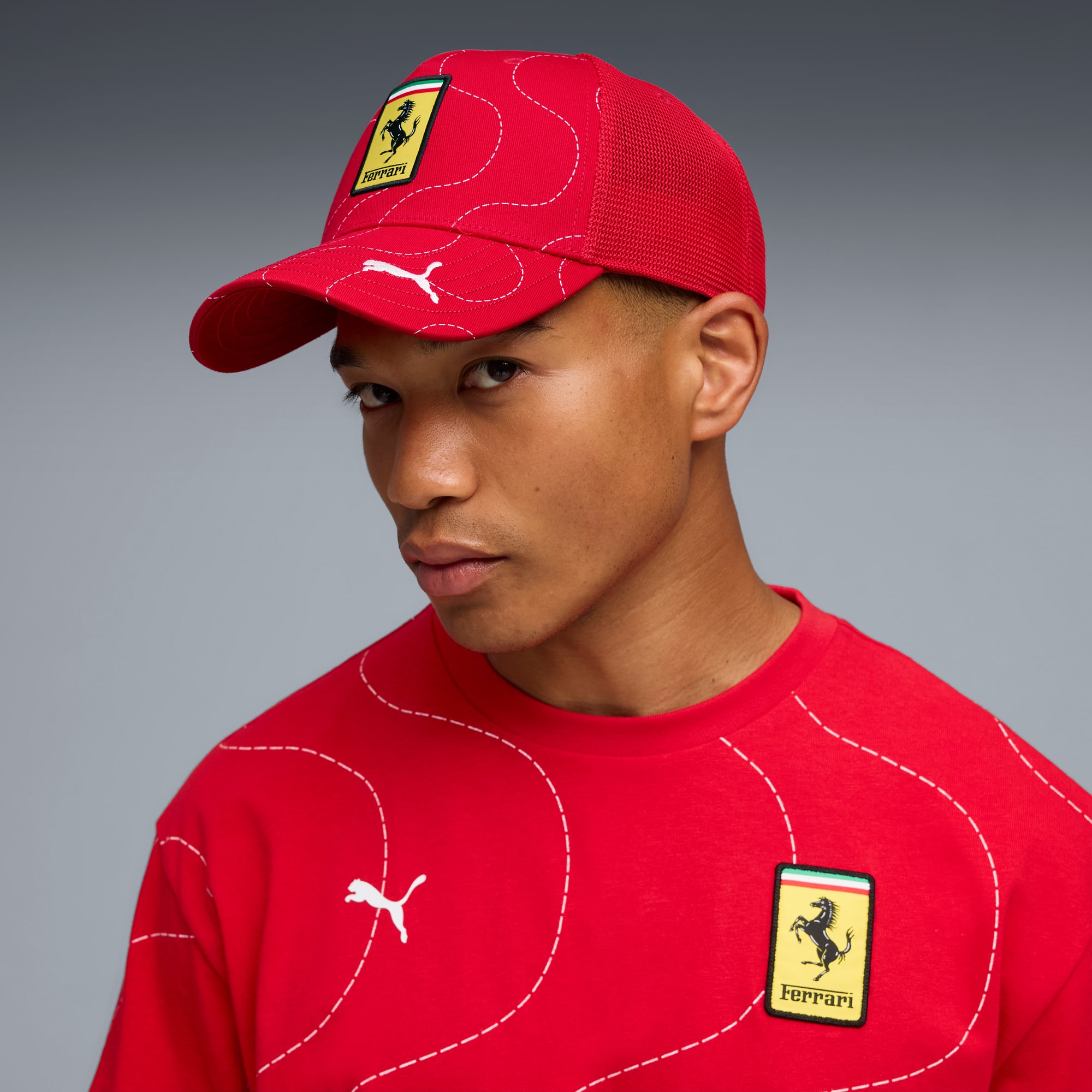 Sur un fond gris, un modèle porte un t-shirt et une casquette rouges de marque Ferrari.
