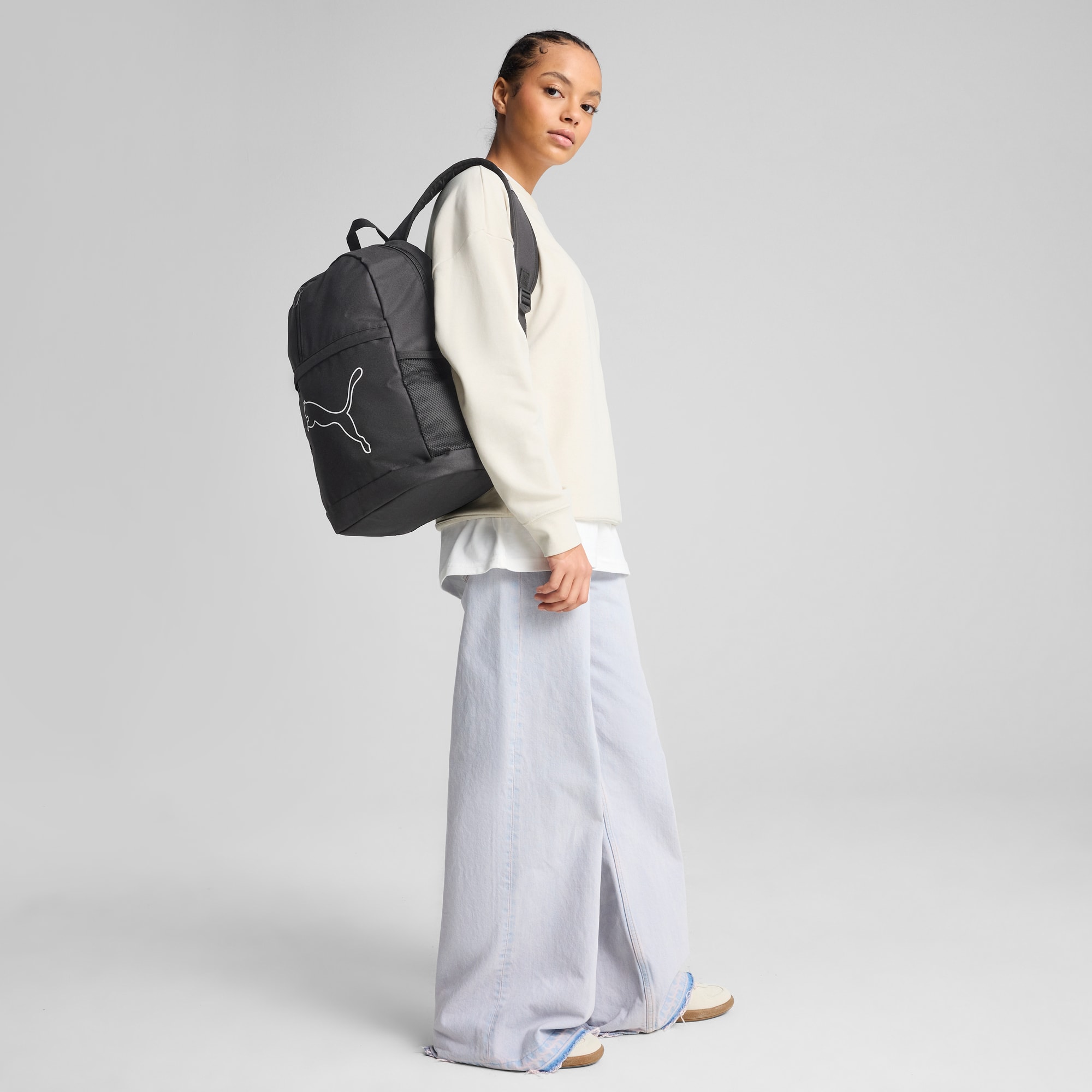 Un mannequin se tient sur un fond gris, portant un sac à dos noir avec un logo blanc.