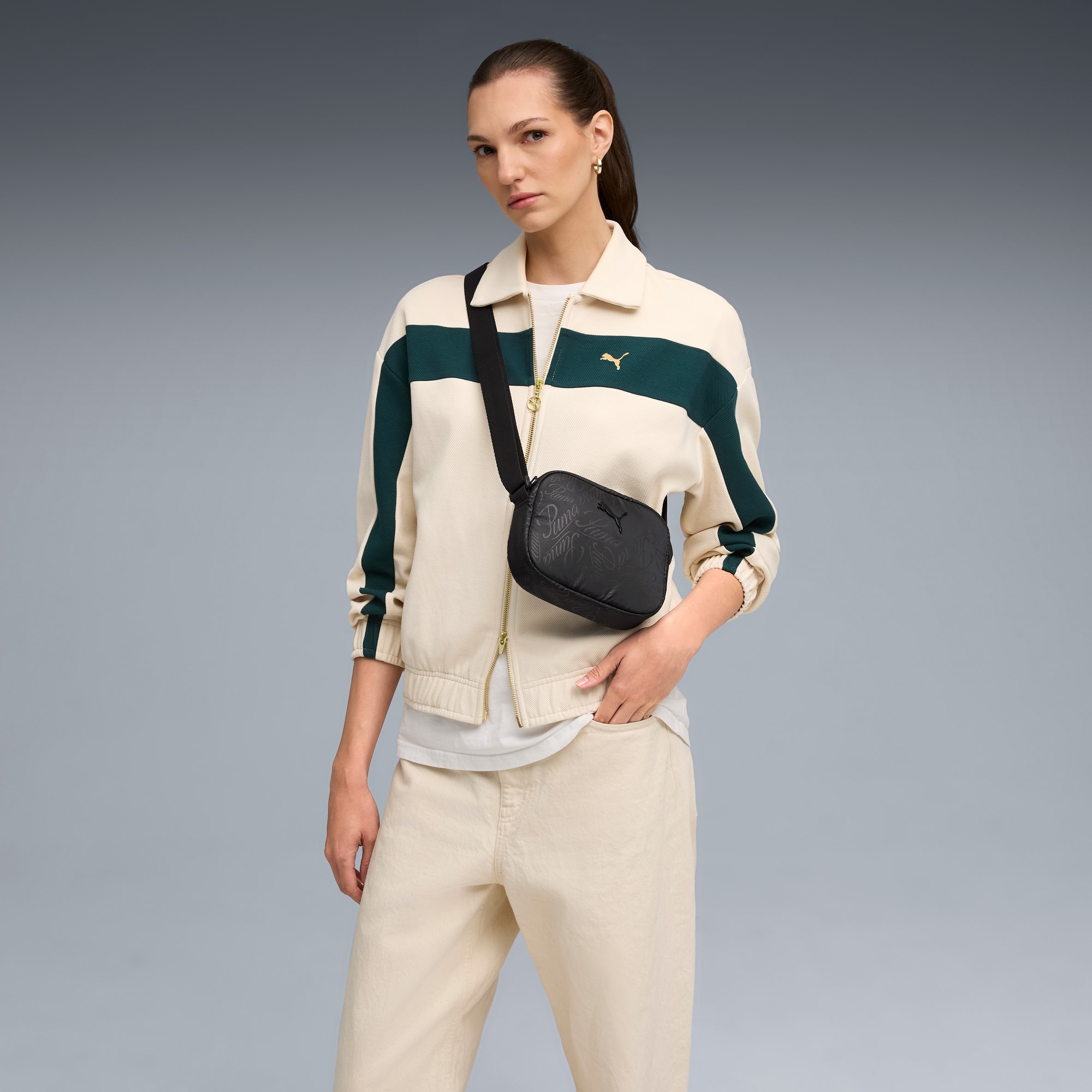Ein Model posiert vor grauem Hintergrund mit Jacke und schwarzer Umhängetasche.