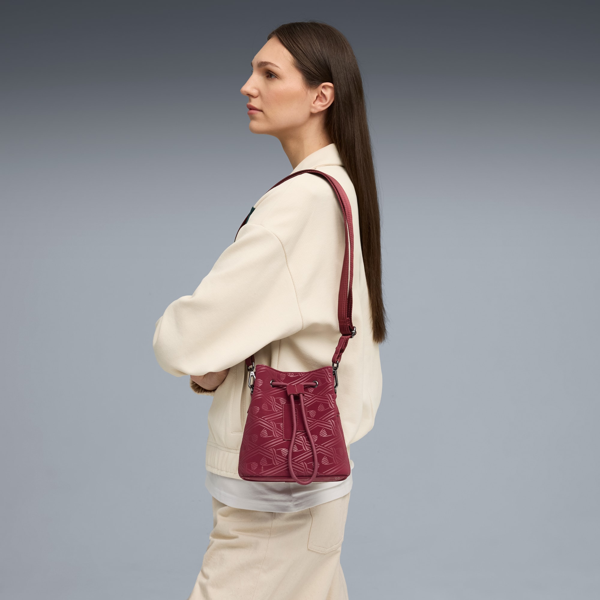 Tegen een grijze achtergrond draagt een model een crèmekleurig jasje met een rode tas met patroon.