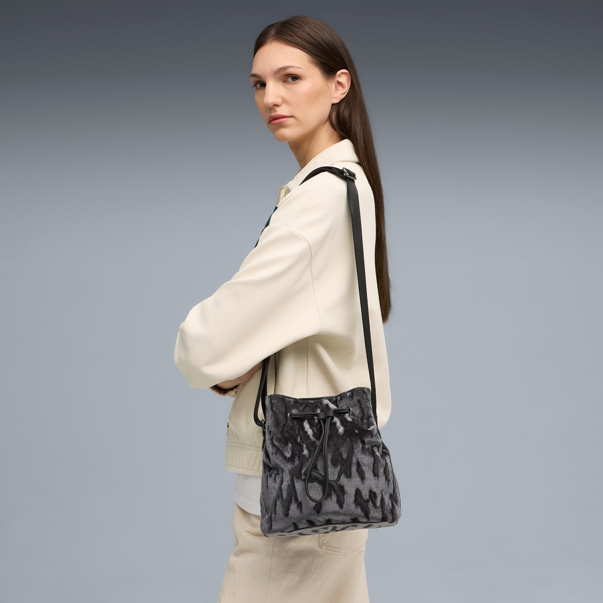 Sobre un fondo gris, una modelo posa con un bolso bombonera estampado y chaqueta clara.