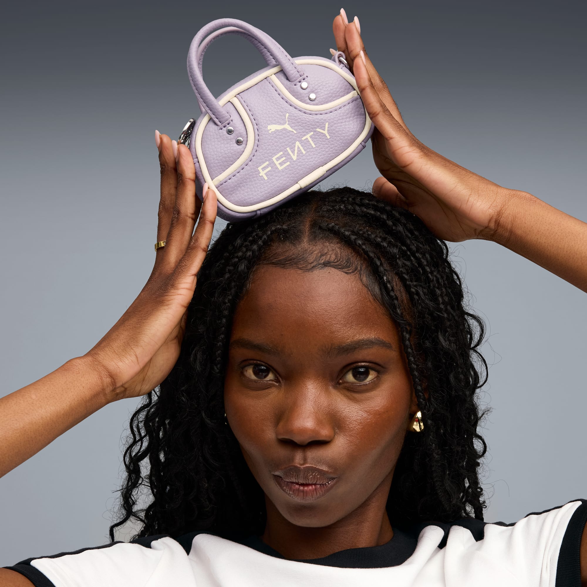Tegen een grijze achtergrond houdt een model een lavendelkleurige Fenty handtas boven haar hoofd.