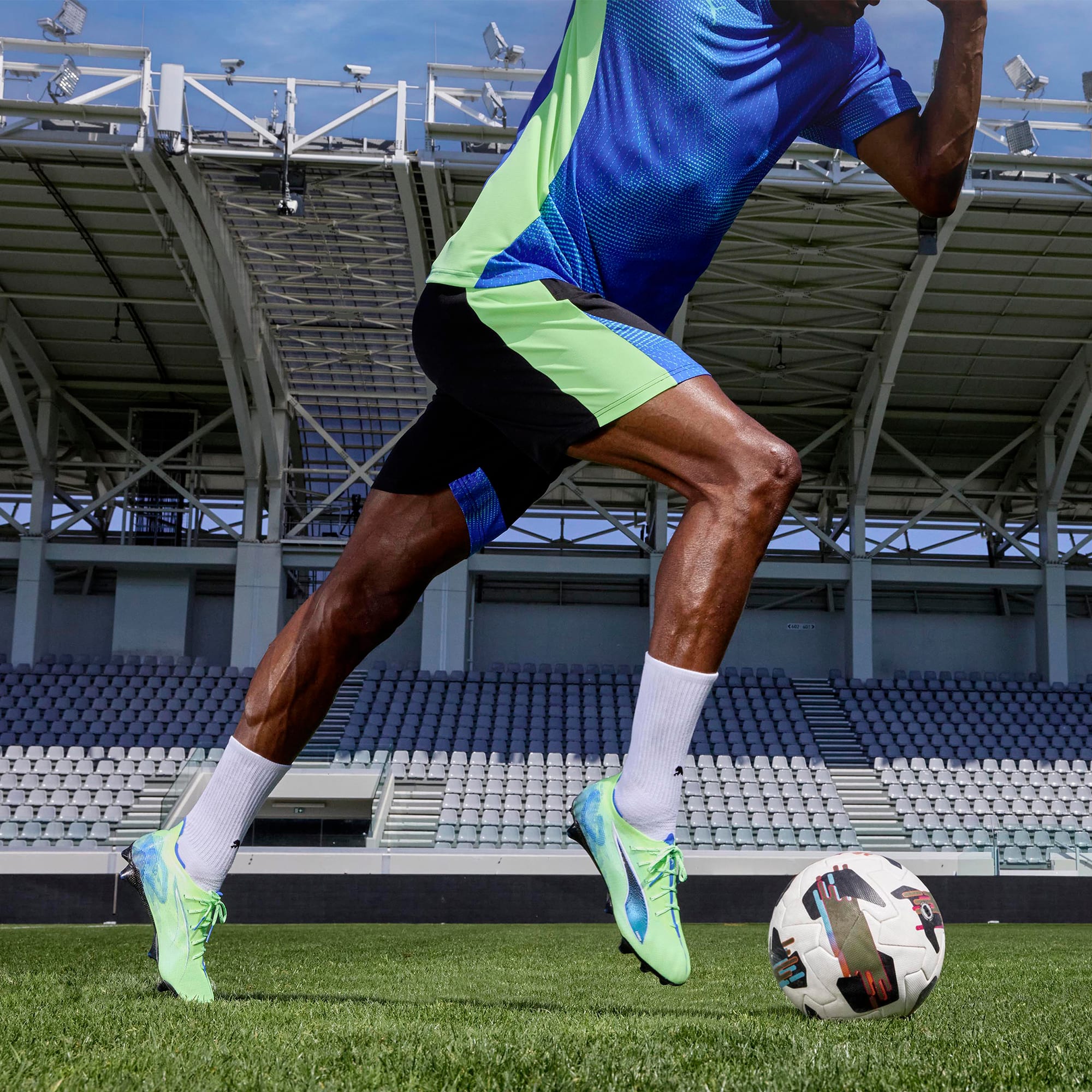 Een model voor stadionstoelen, dat rent om een voetbal te trappen, gekleed in een blauwgroen t-shirt.