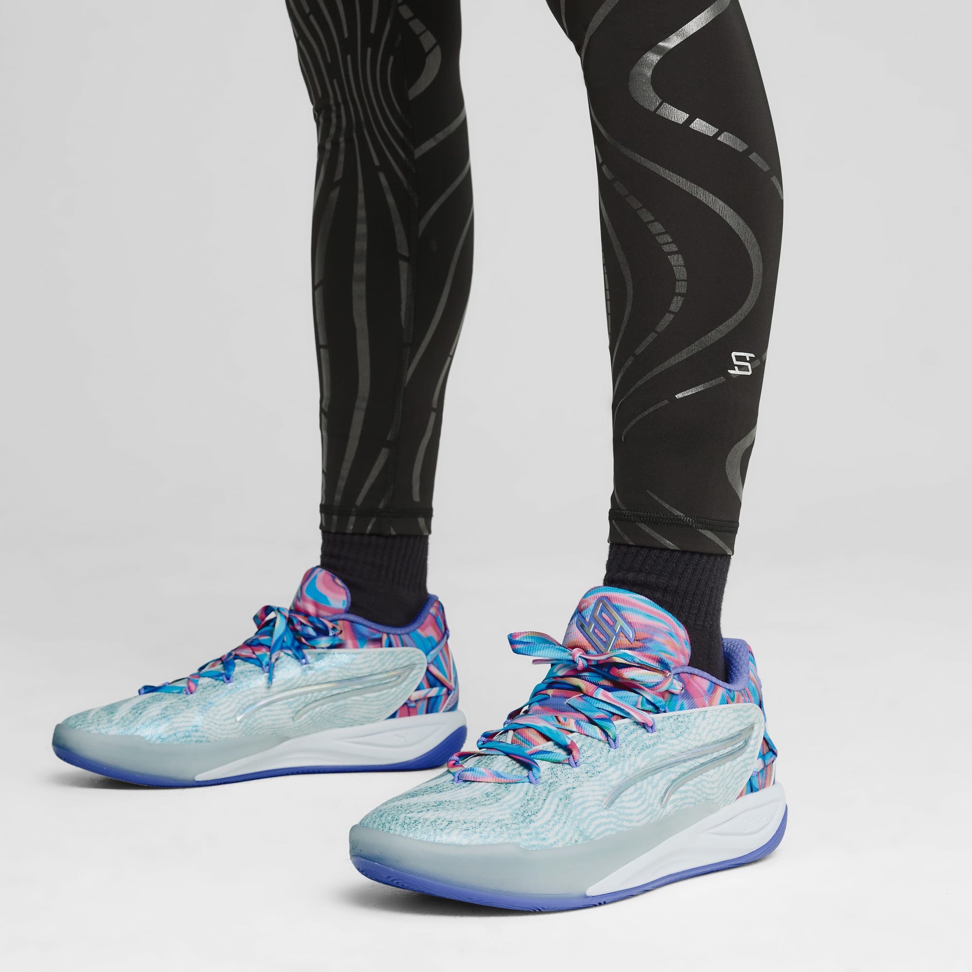 Op een grijze achtergrond draagt een model een legging met print en kleurrijke hardloopschoenen.