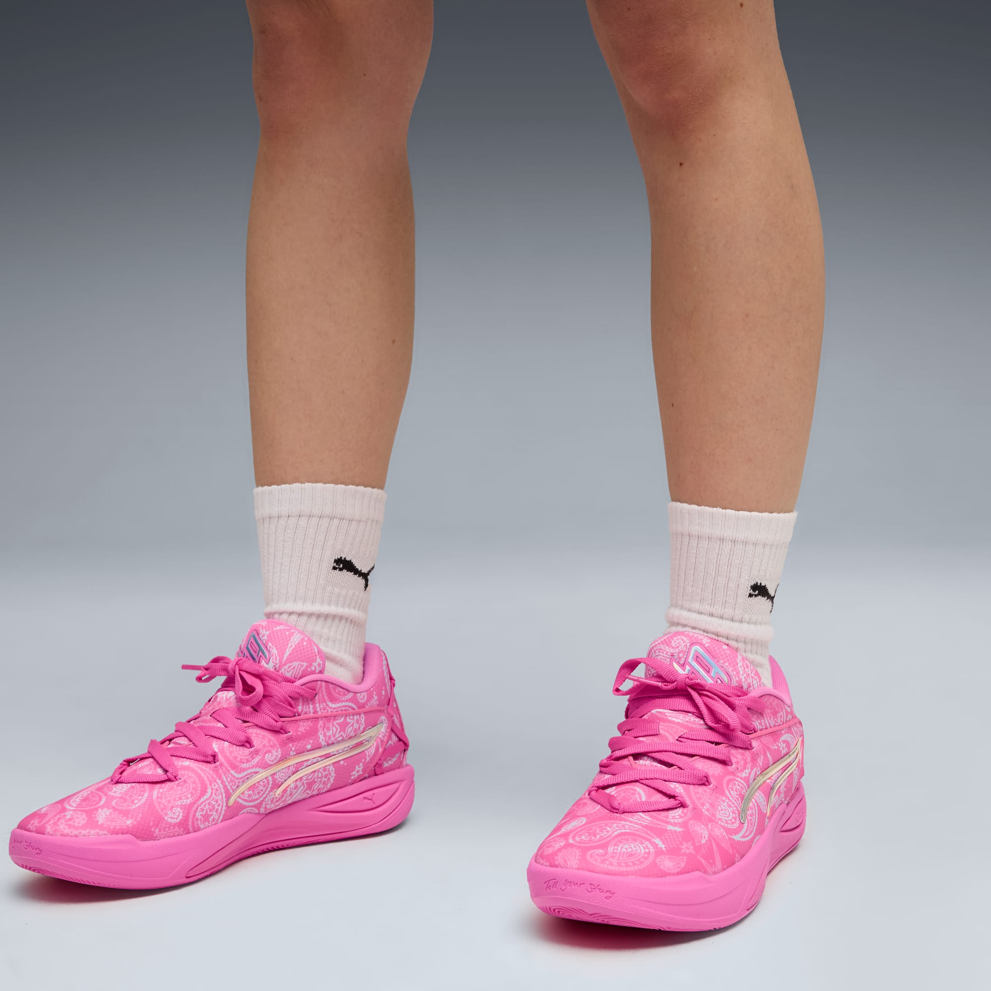 Su uno sfondo grigio, un modello mostra scarpe da ginnastica rosa fantasia e calzini bianchi.