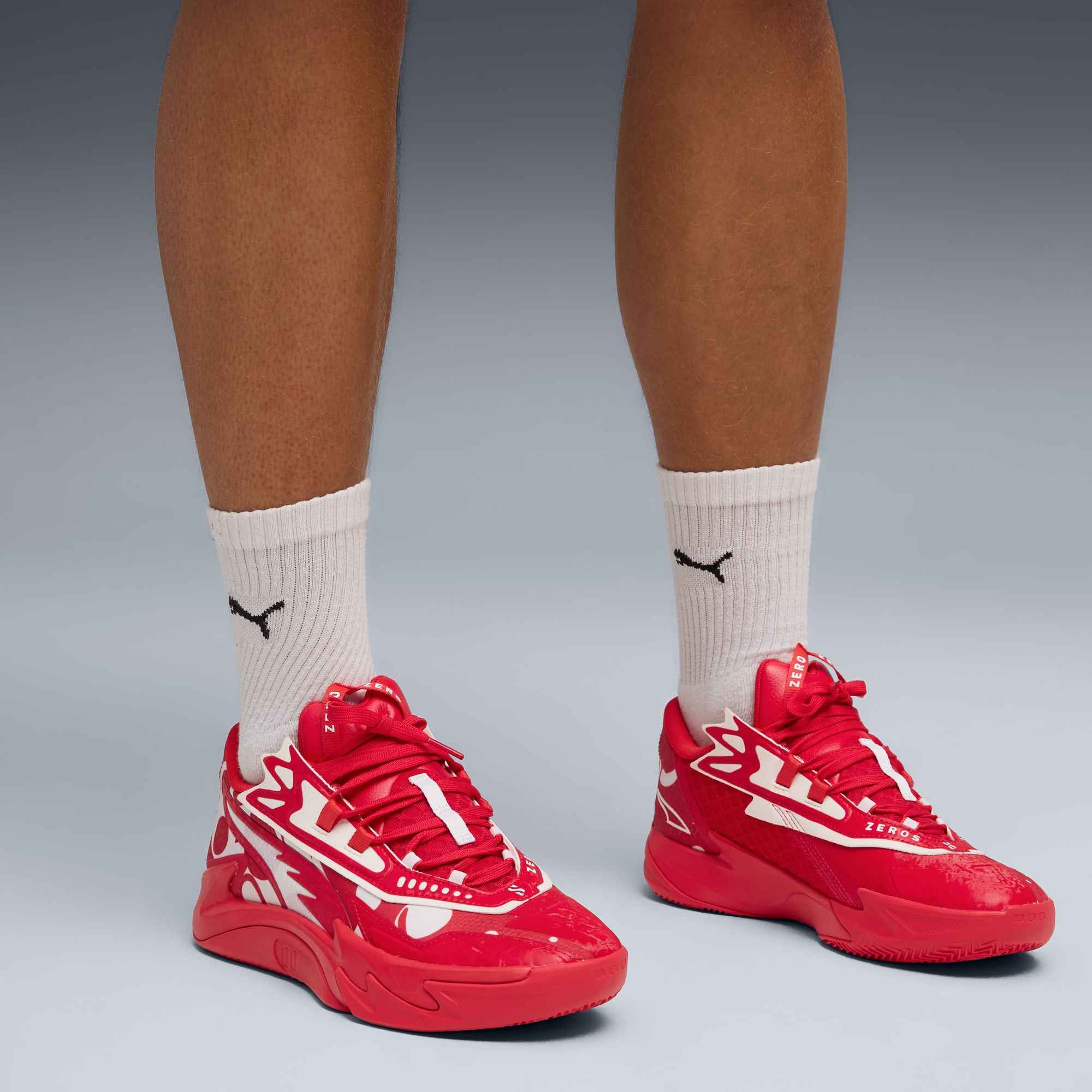 Su sfondo grigio, un modello indossa scarpe da ginnastica rosse e calzini bianchi con logo.