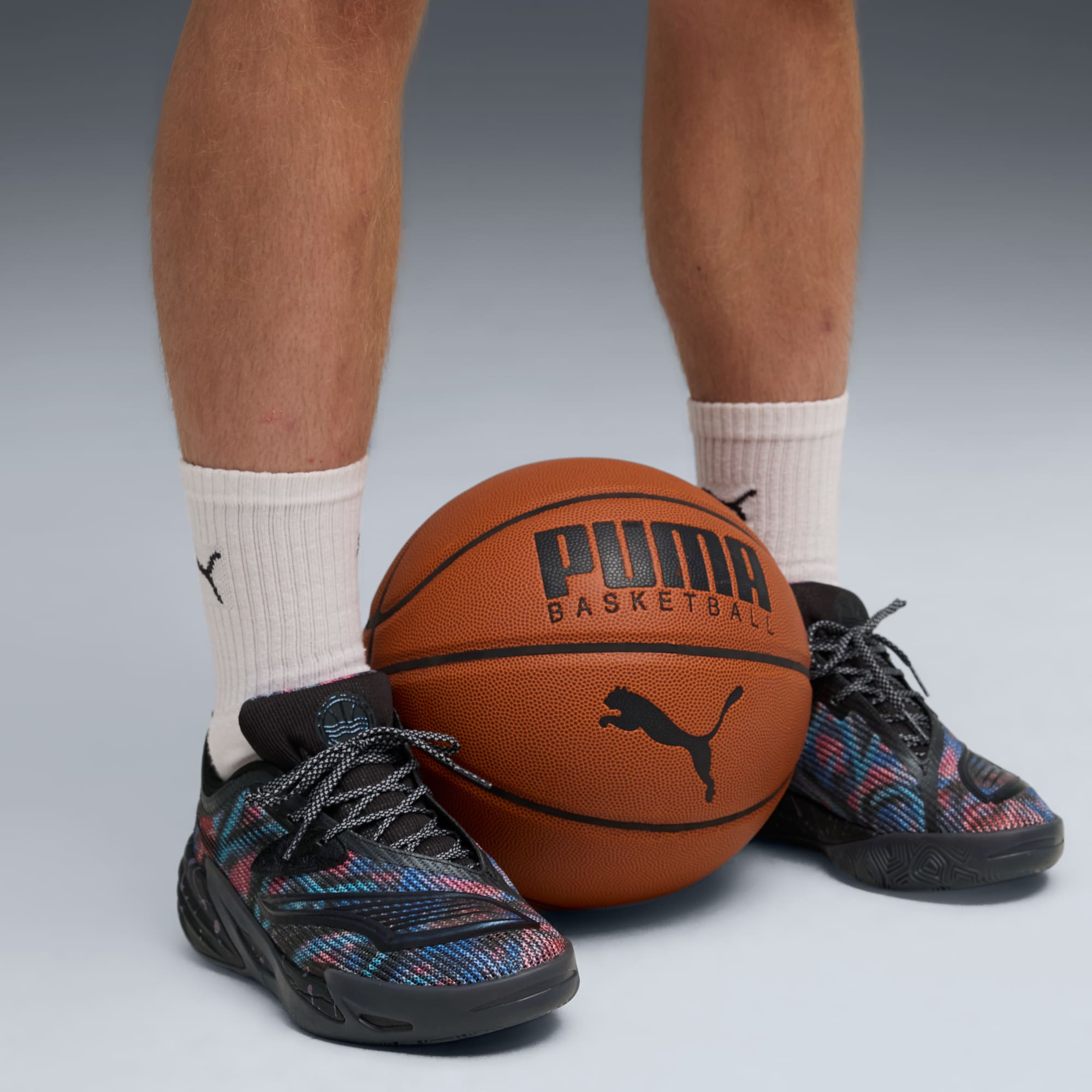 Vor grauem Hintergrund posiert ein Model mit Basketball und gemusterten Puma-Turnschuhen.