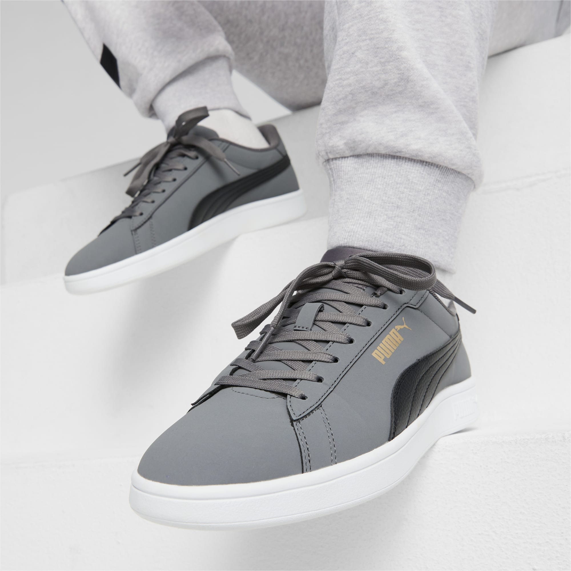 On a white surface, someone wears grey trainers with black detail and grey jogging bottoms.