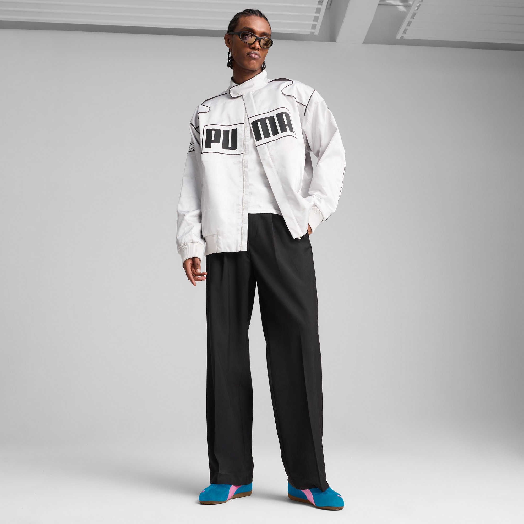 Un mannequin pose sur fond gris, portant veste de marque, pantalon et baskets.