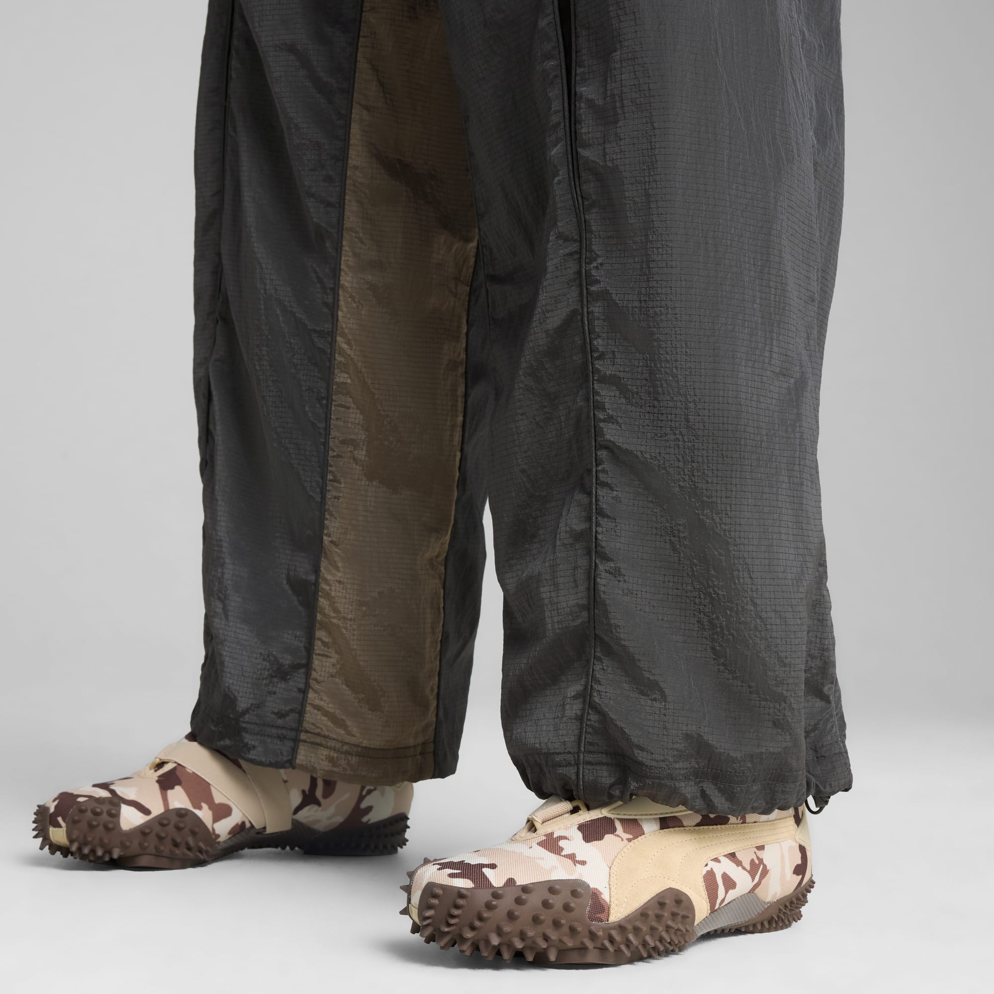 Su sfondo grigio, una persona indossa scarpe da ginnastica mimetiche e pantaloni larghi bicolore.