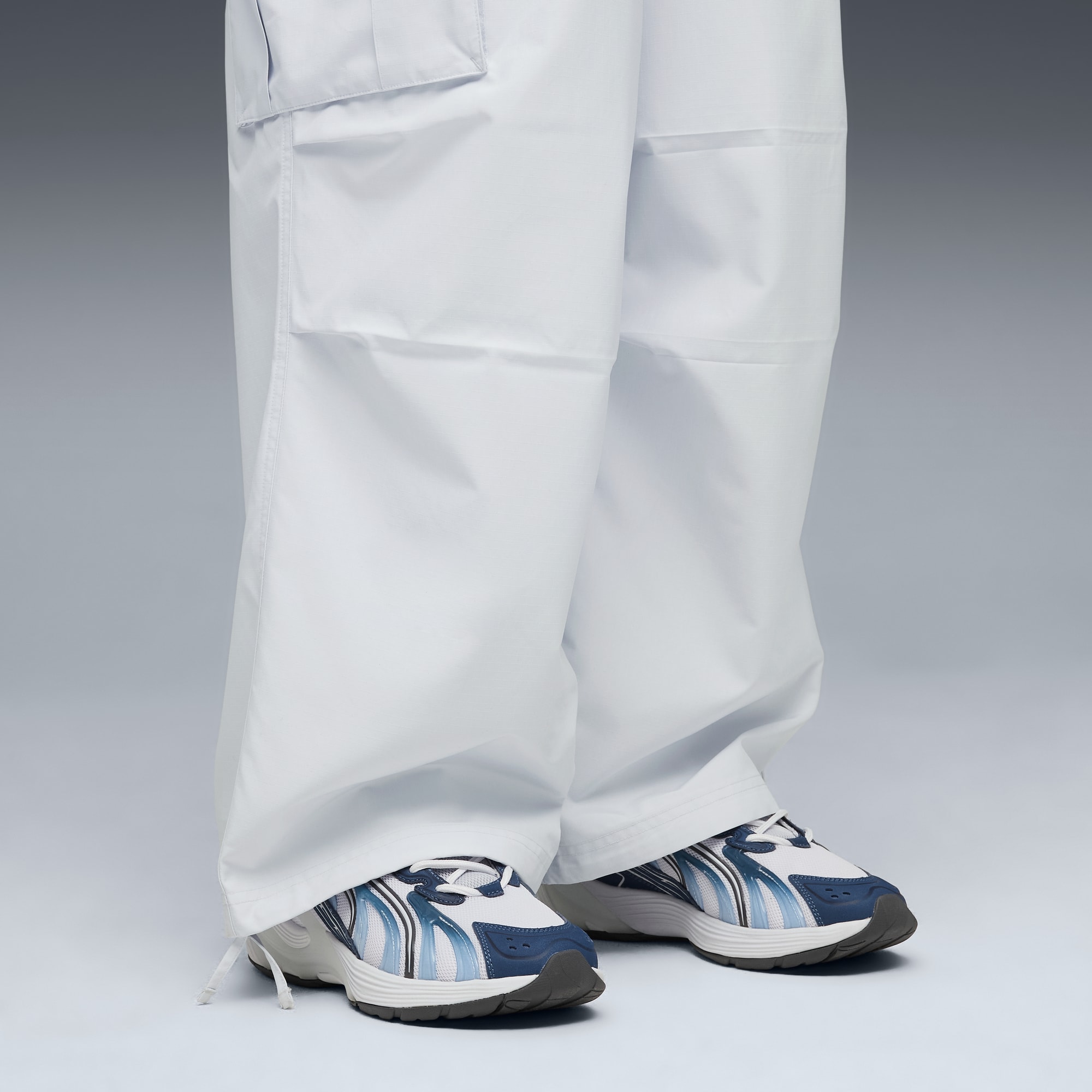 Tegen grijs draagt een model een witte broek en sportschoenen in een loopbeweging.