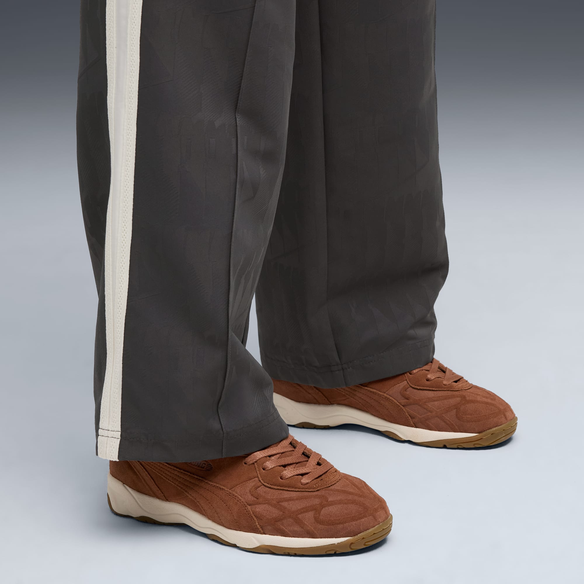 Su uno sfondo grigio, una persona indossa pantaloni grigi e scarpe da ginnastica marroni.