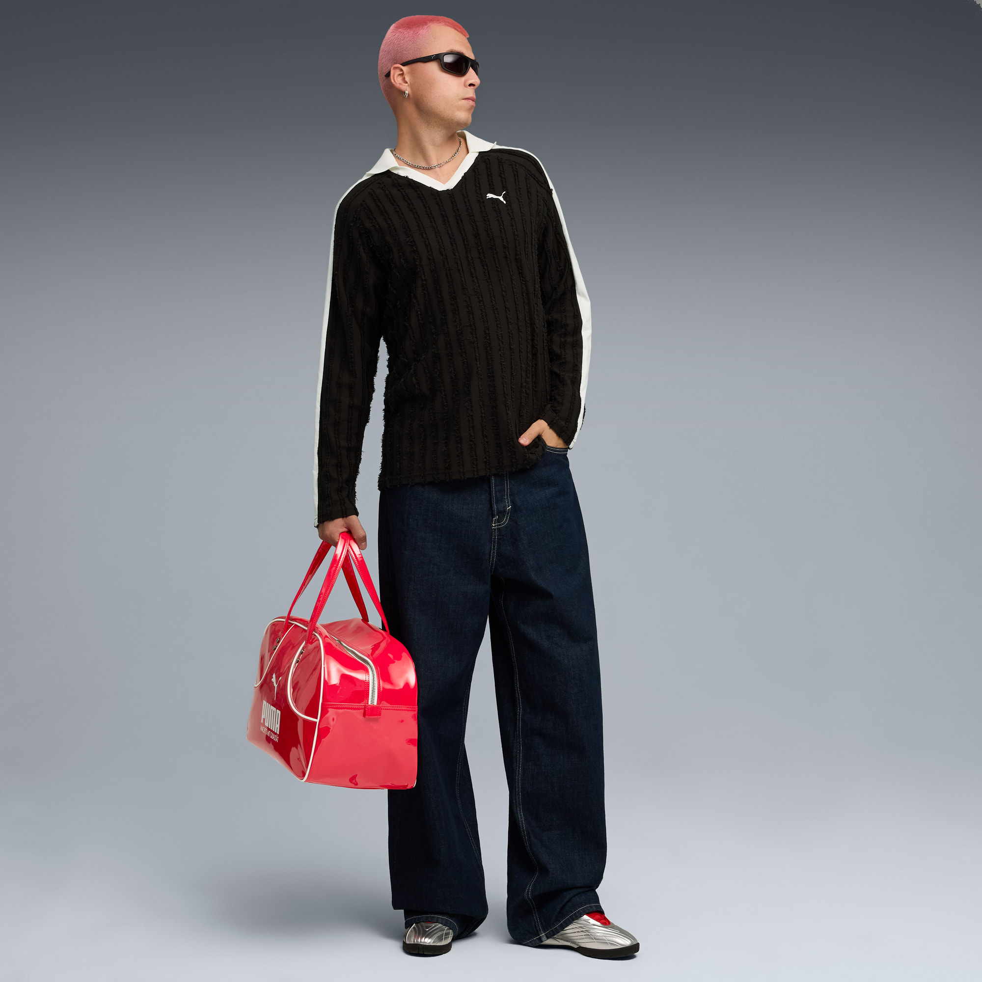 Un mannequin aux cheveux roses pose avec un sac rouge, un haut noir et un jean large.