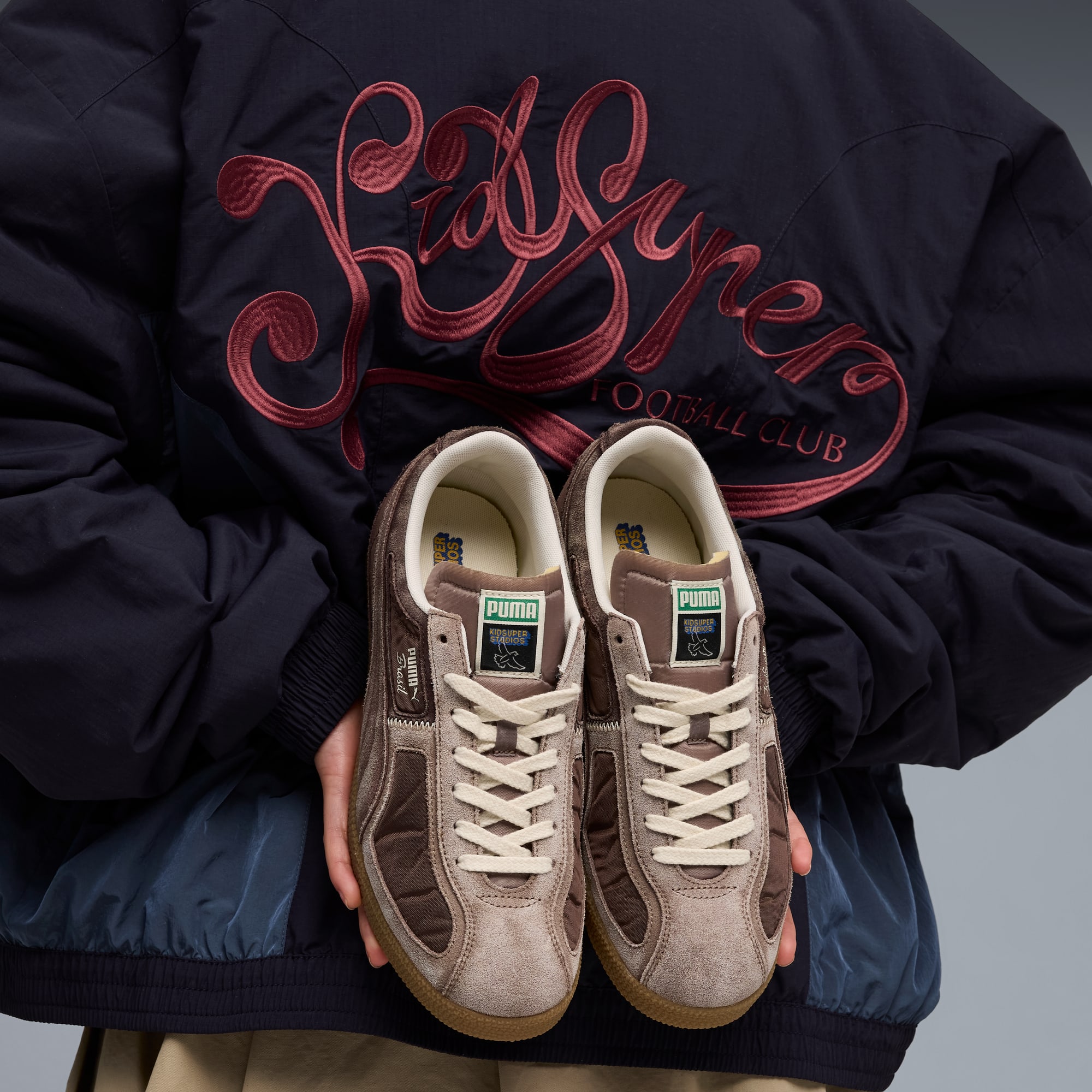 Una chaqueta bordada sostiene zapatillas marrones con cordones sobre un fondo gris.