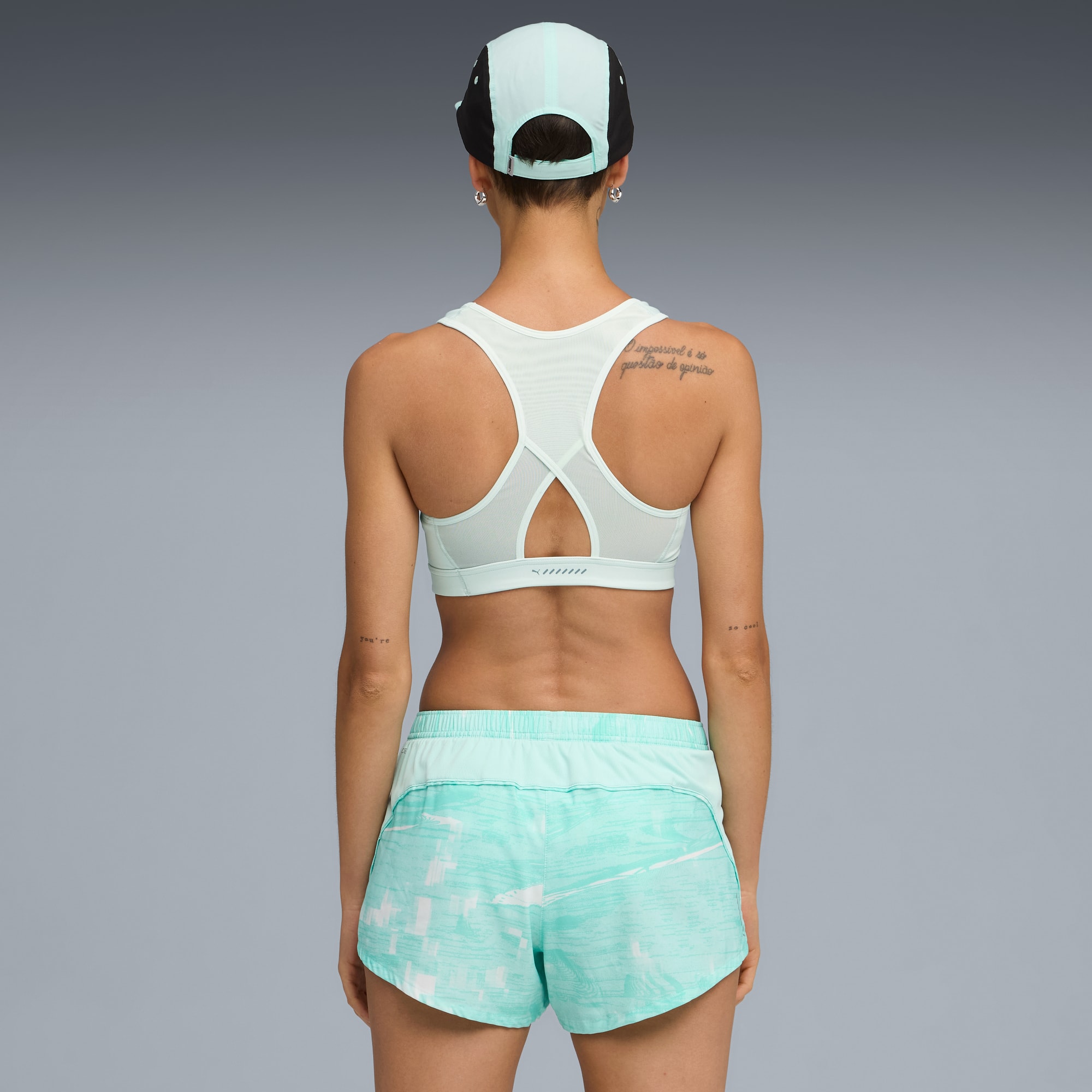 Ein Model mit Sport-BH und Shorts steht vor grauem Hintergrund.