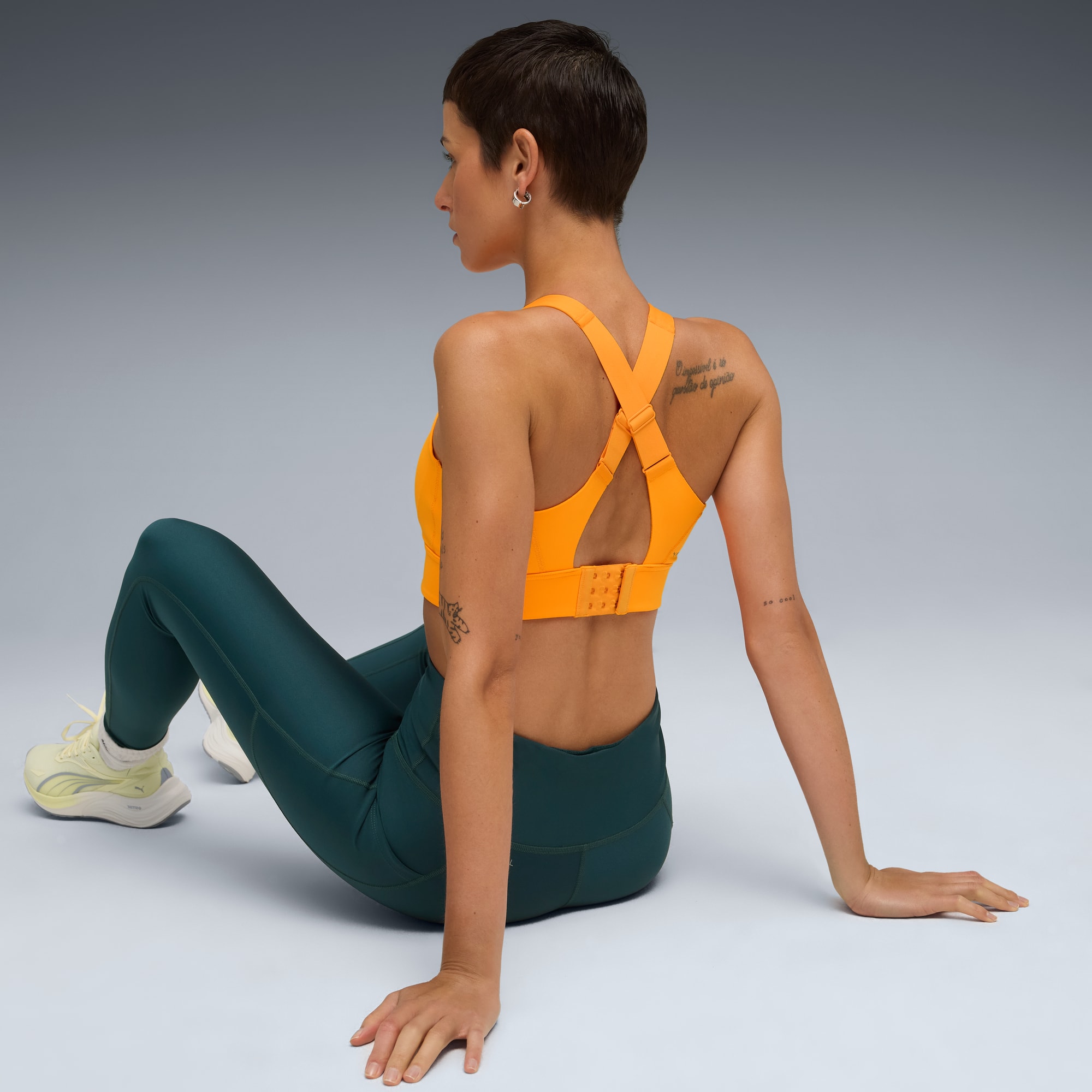 Un mannequin est assis sur fond gris, portant un haut orange et un legging vert.