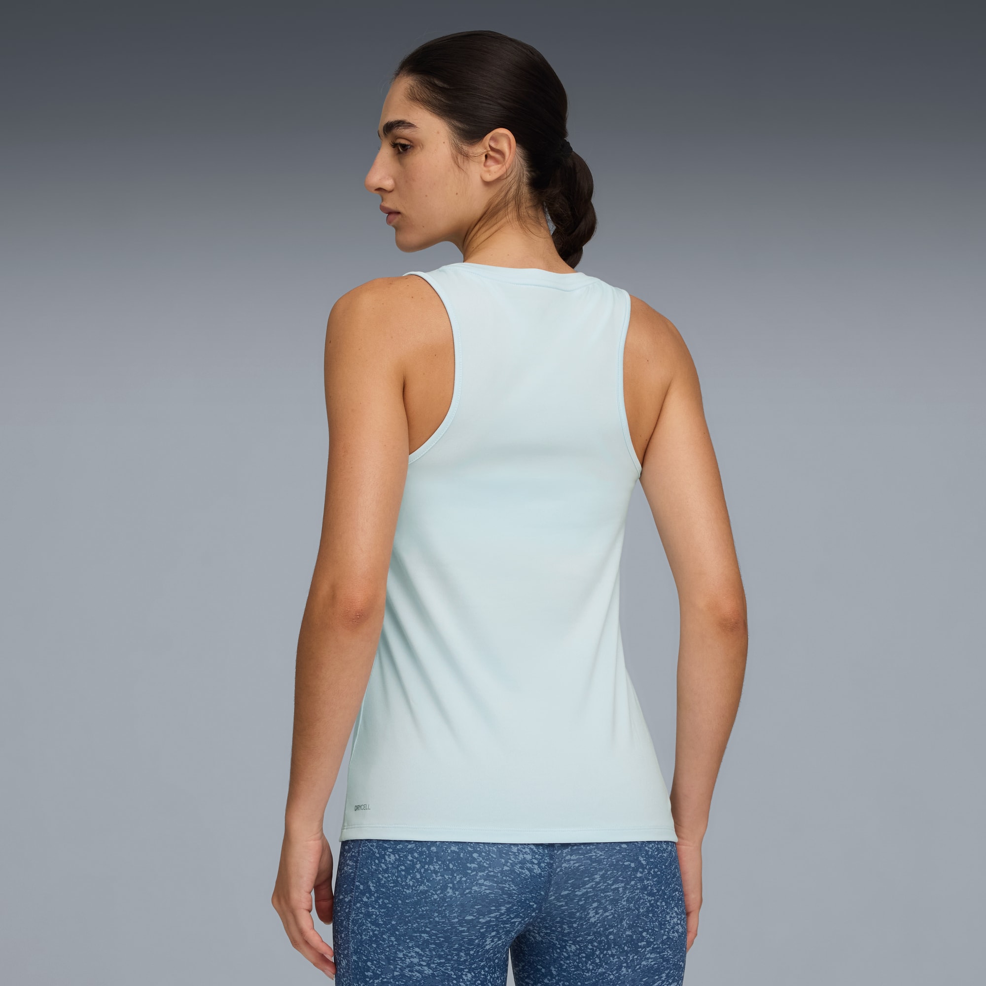 Su sfondo grigio, modella di spalle con canotta azzurra e leggings blu fantasia.